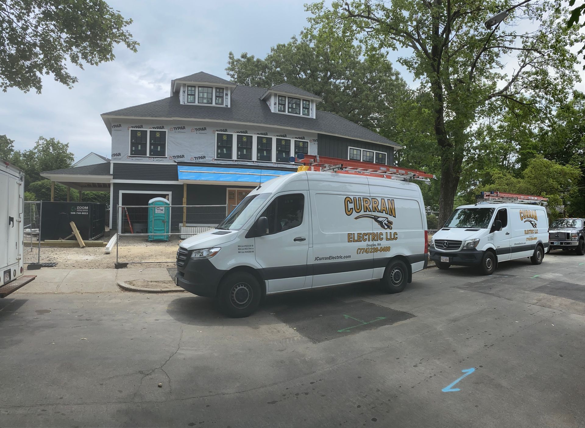 White work vans with company logo parked outside a two-story house under construction.
