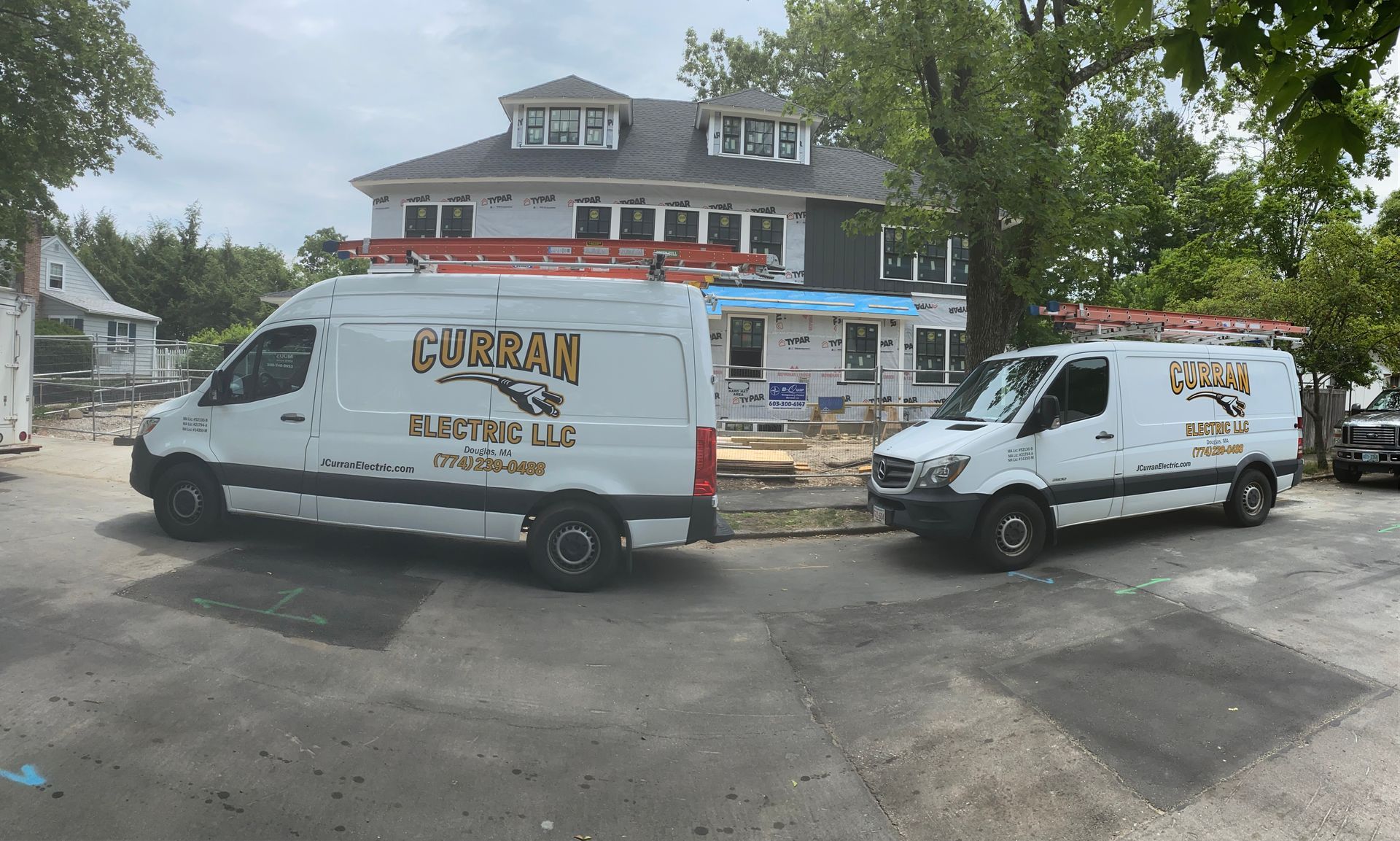 Two white work vans parked in front of a house under construction; the vans display 