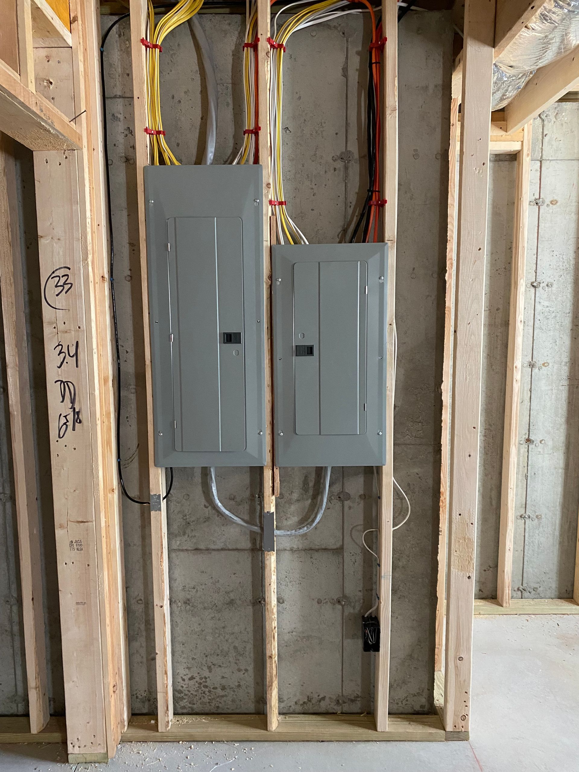 Two gray electrical panels mounted on a wooden frame against a concrete wall. Wiring is visible.