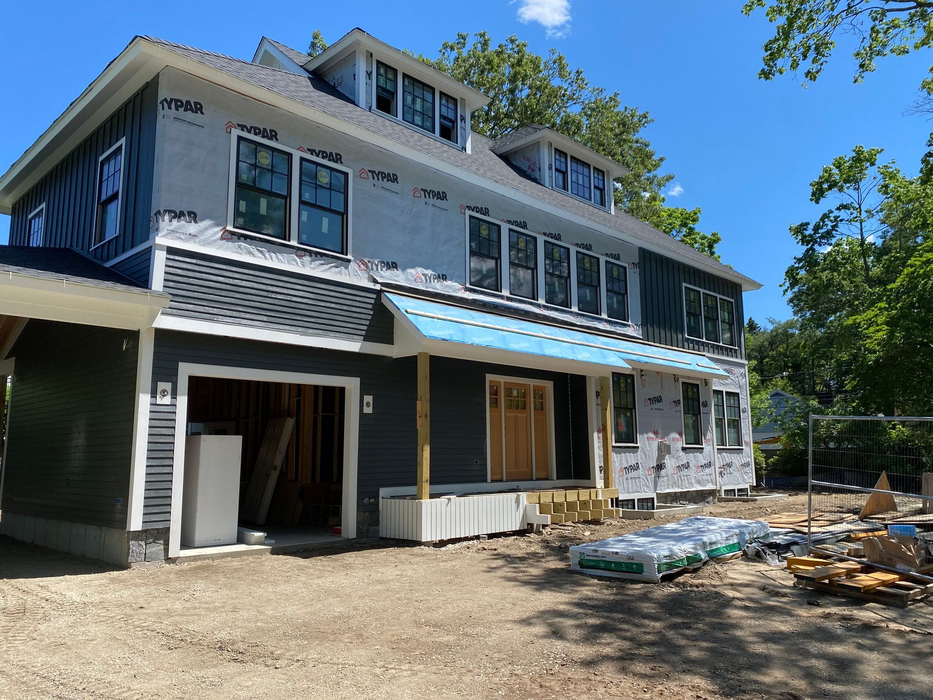 Two-story house under construction with dark siding, unfinished windows, and a garage; outdoors on a sunny day.