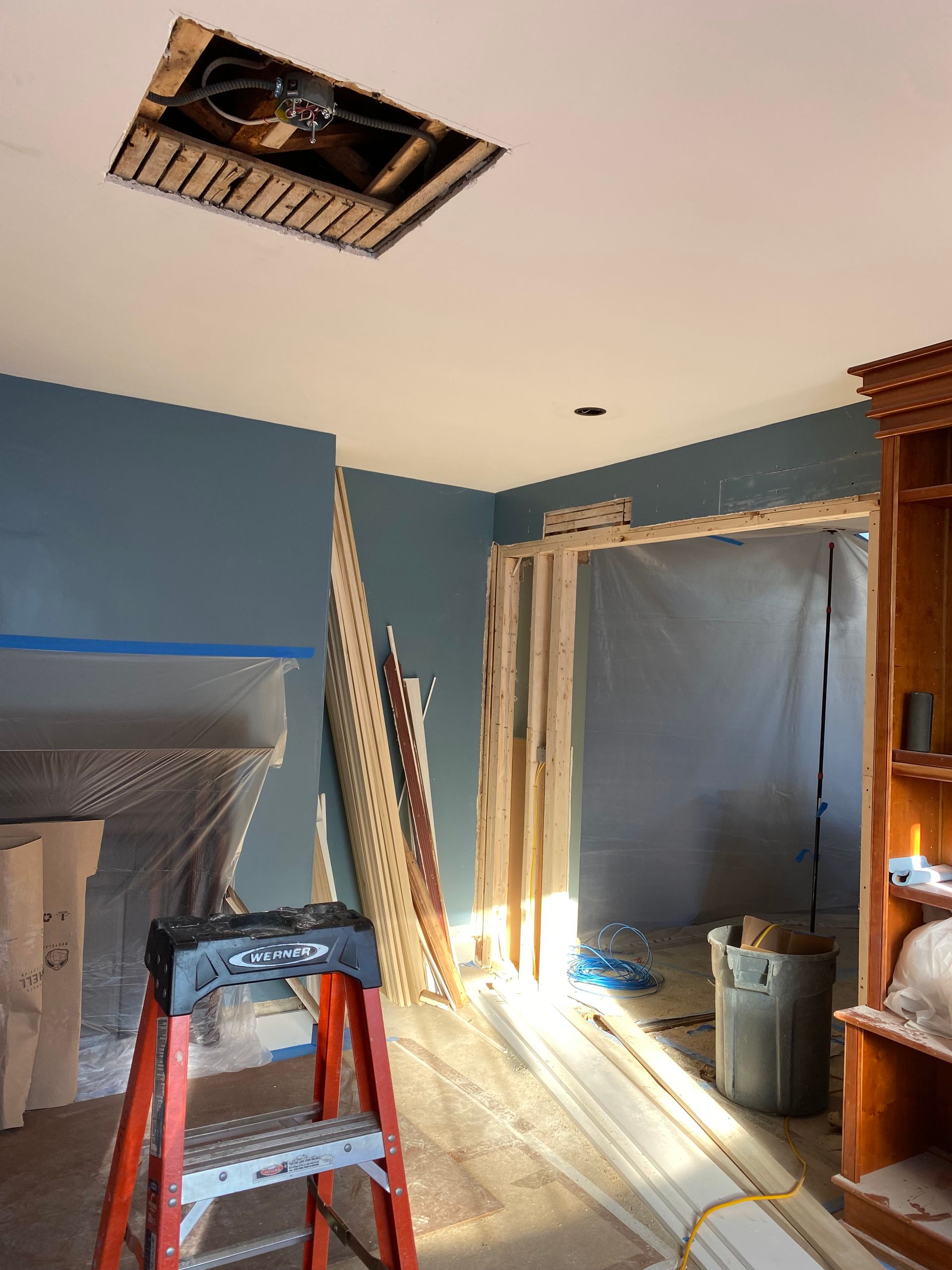 Room under renovation with blue walls, open ceiling, ladder, and plastic sheeting.