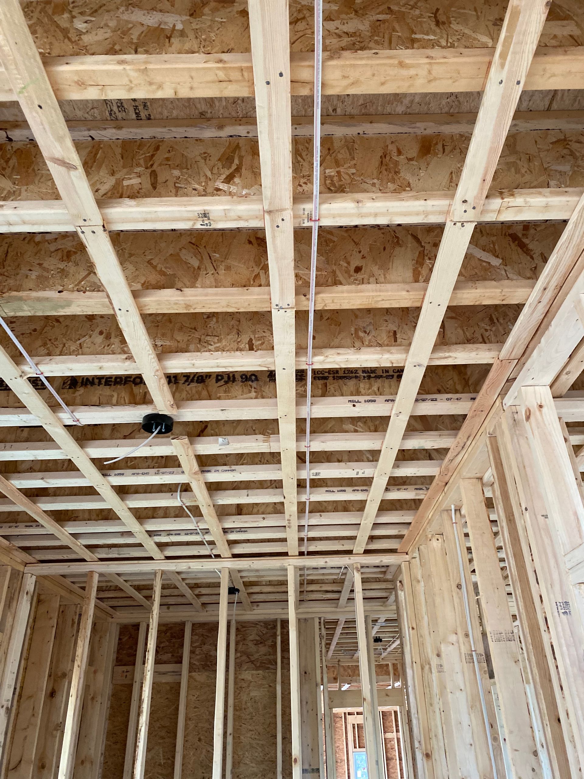 Interior of a building under construction, showing wooden framing and ceiling joists with electrical wiring.