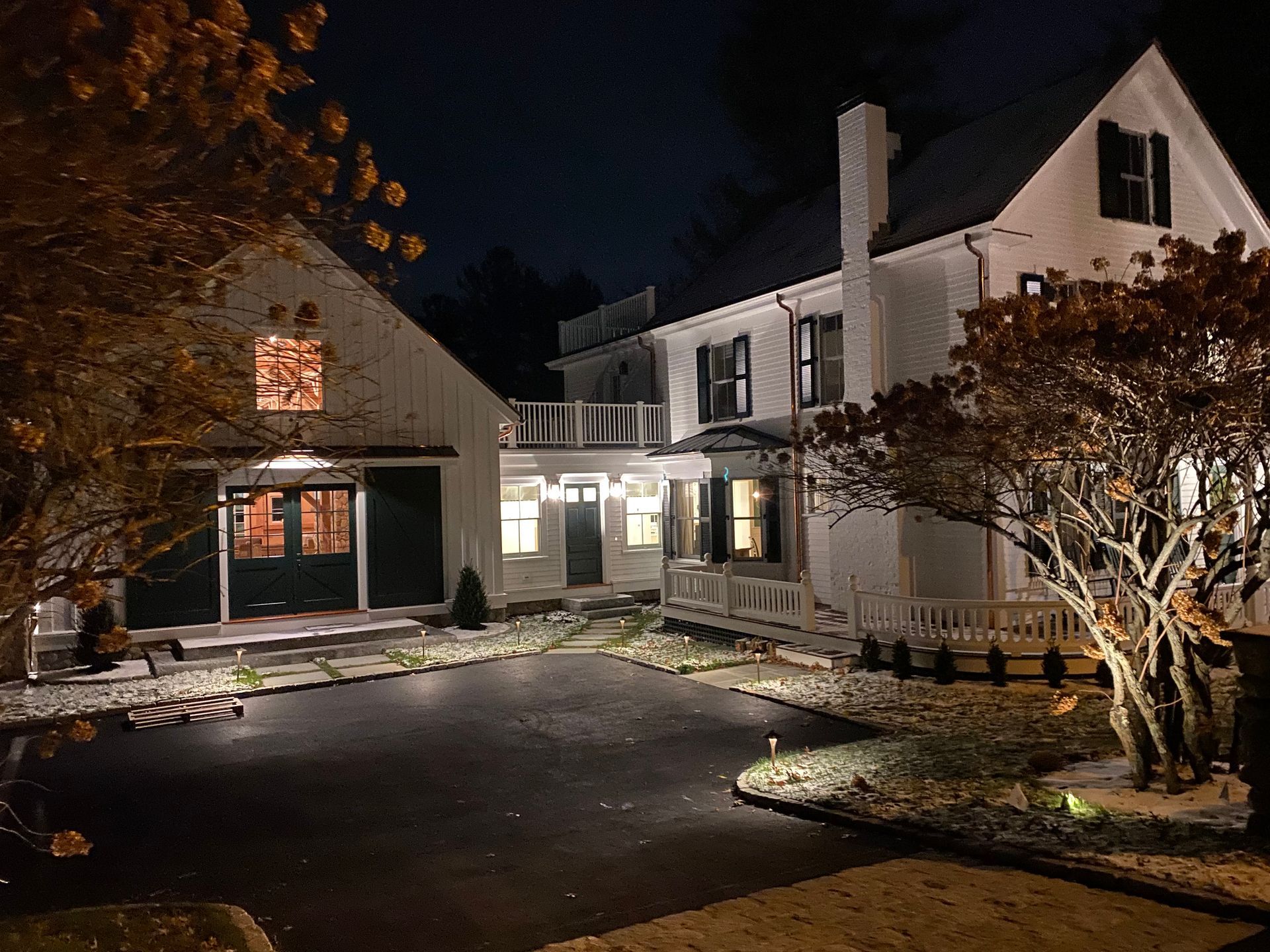 White house and barn at night, with lit windows and a dark driveway.