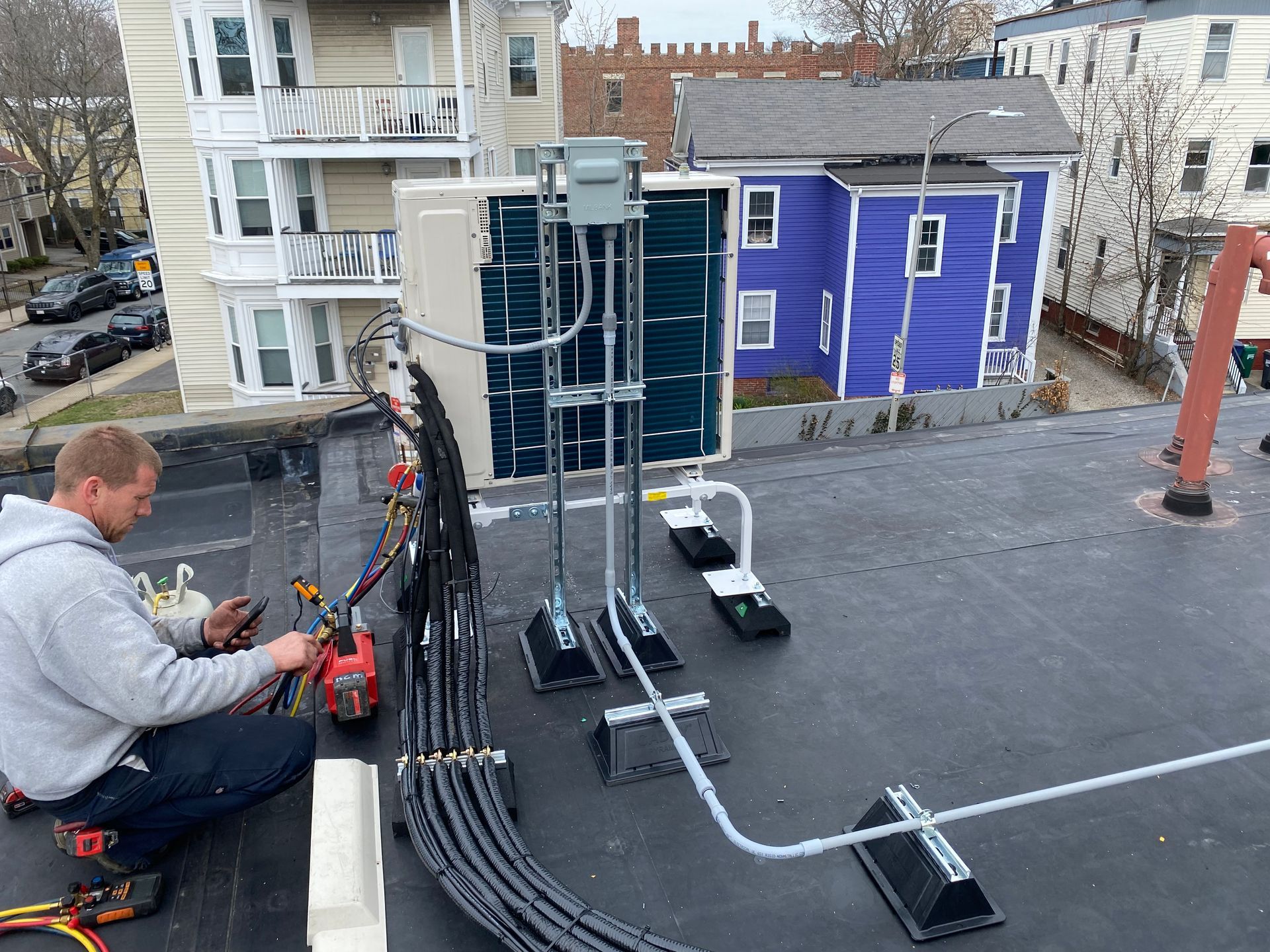 Man working on rooftop HVAC unit, wiring tools in hand. Grey and black cables run along roof.