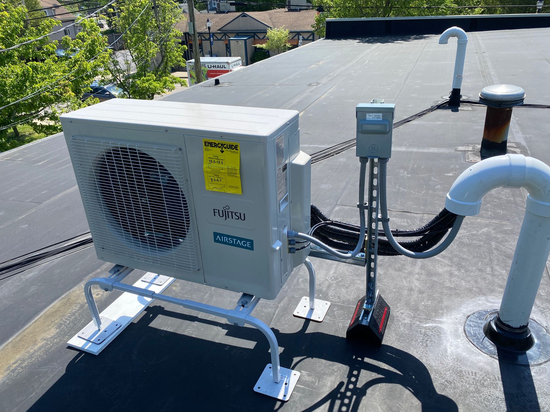 HVAC unit on a rooftop, supported by a metal frame. Black roof with white vents and pipes.