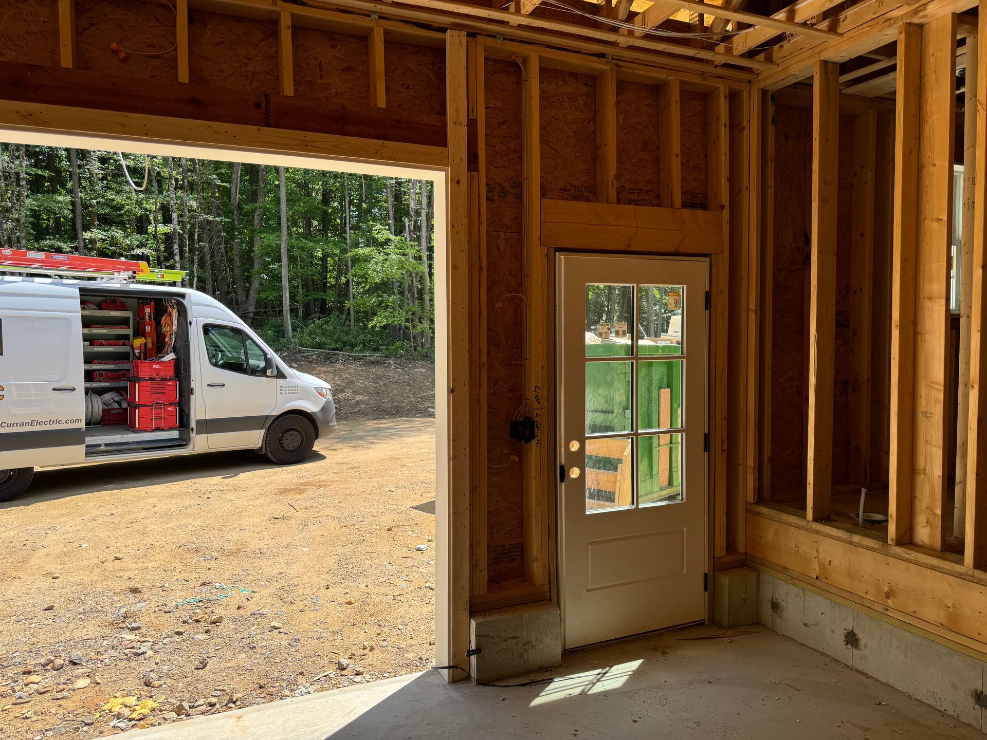 Interior of a garage under construction with a white work van in the driveway.