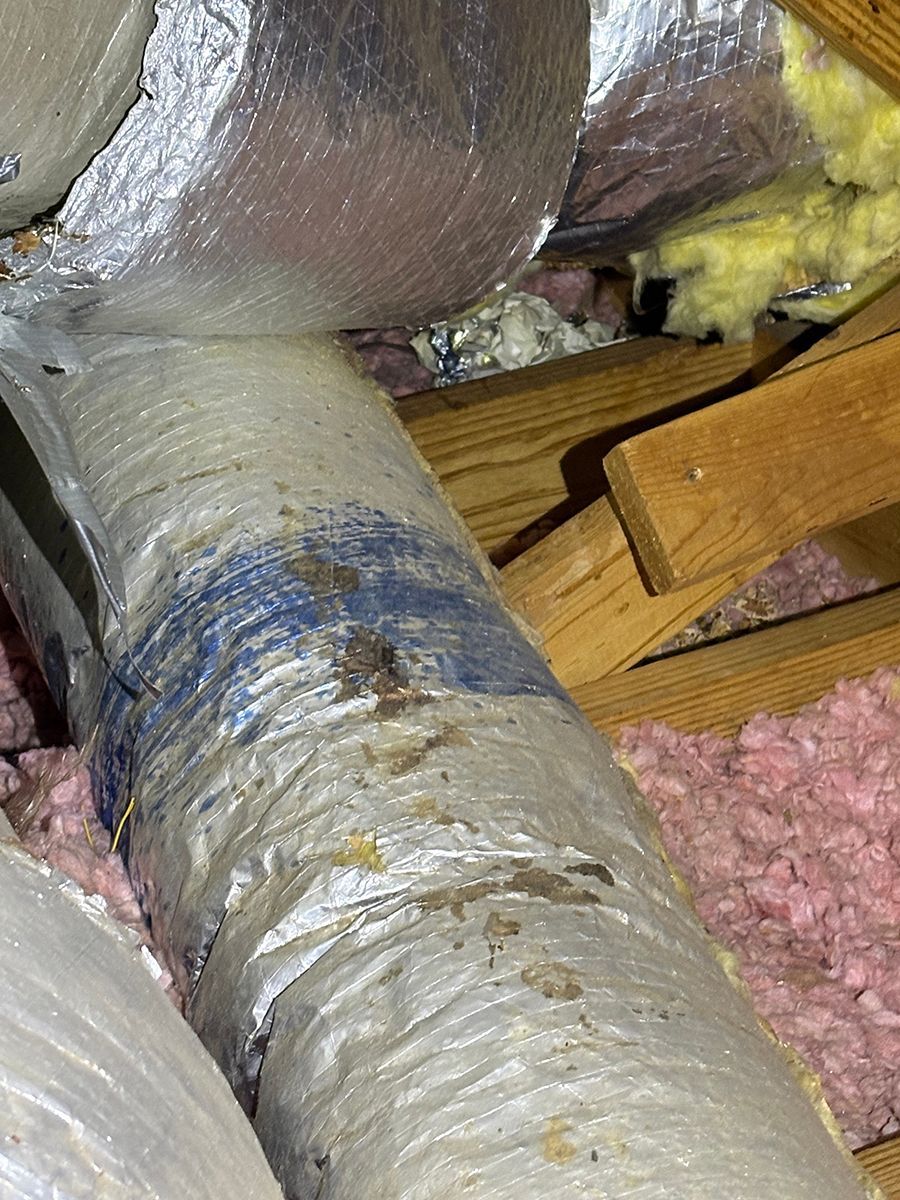 Foil-wrapped HVAC ductwork in an attic beside yellow insulation and exposed wooden framing