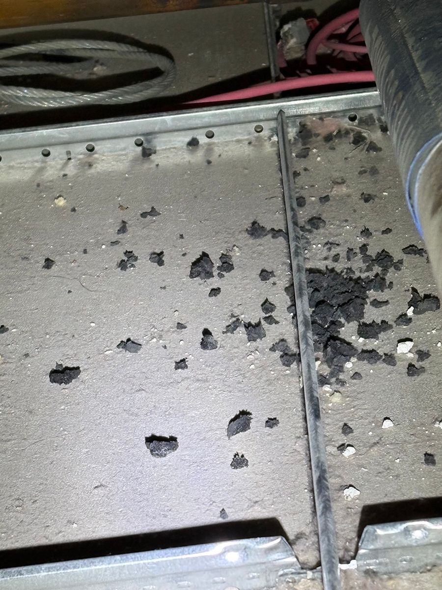 Close-up of dirty metal surface with scattered black debris and a seam line