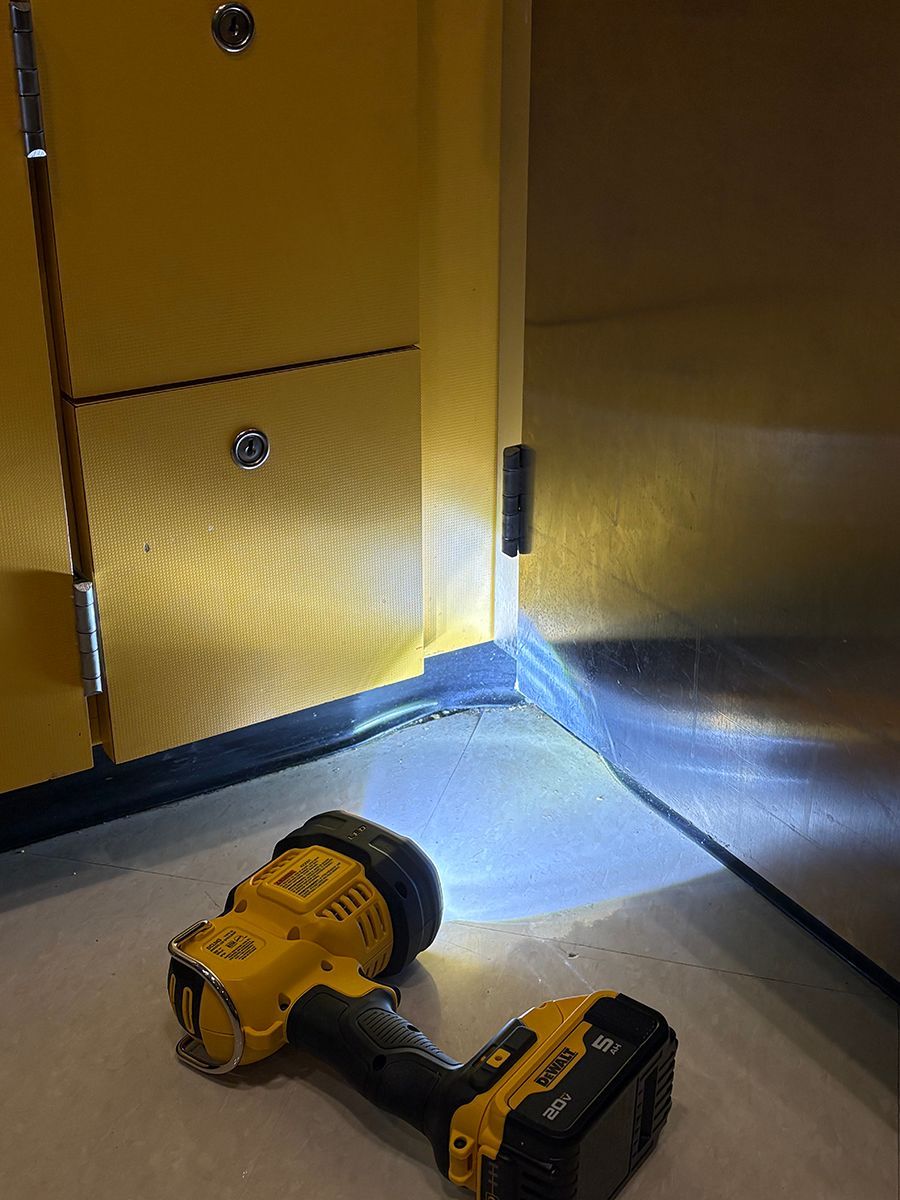 Yellow cordless drill on a gray floor beside yellow cabinets, with a bright flashlight beam shining across the room.