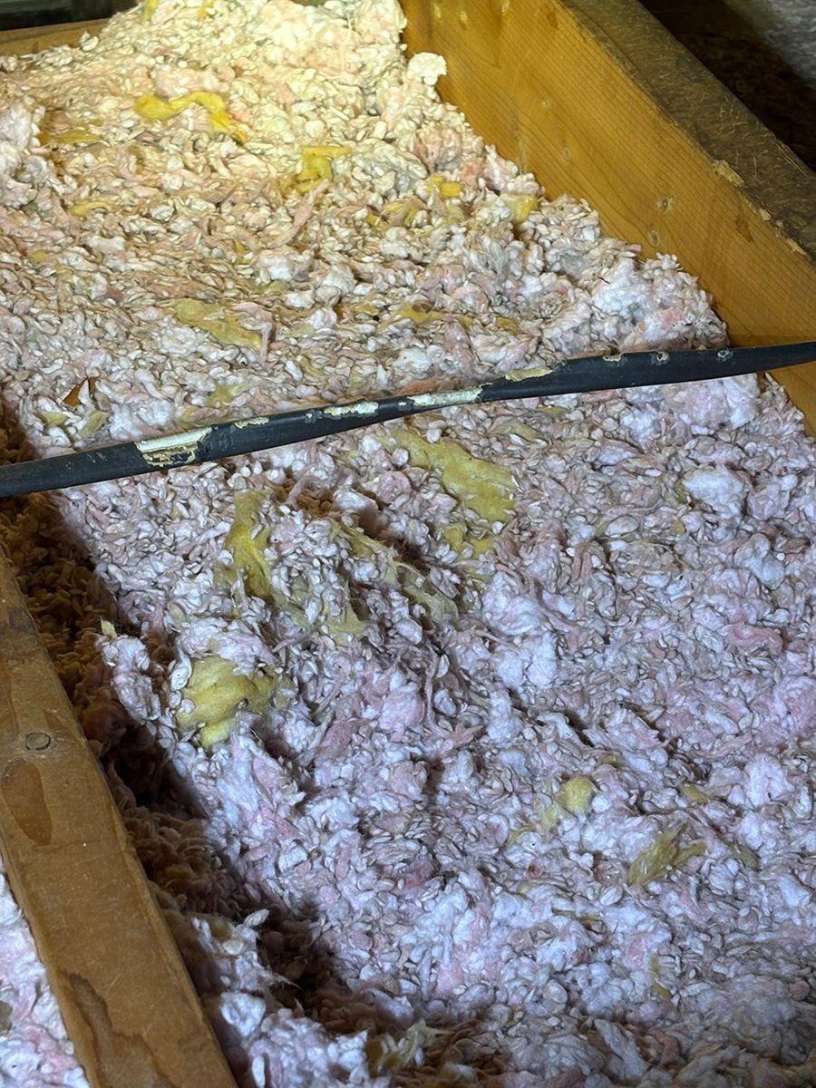 Insulation-filled wooden crawlspace with a black pipe running across it