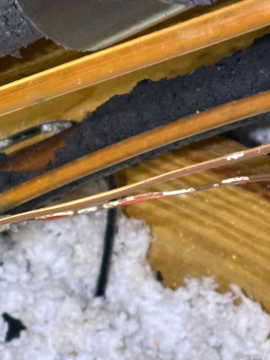 Close-up of a brown wooden edge with dark fabric, a thin wire, and a clump of white stuffing on wood floor