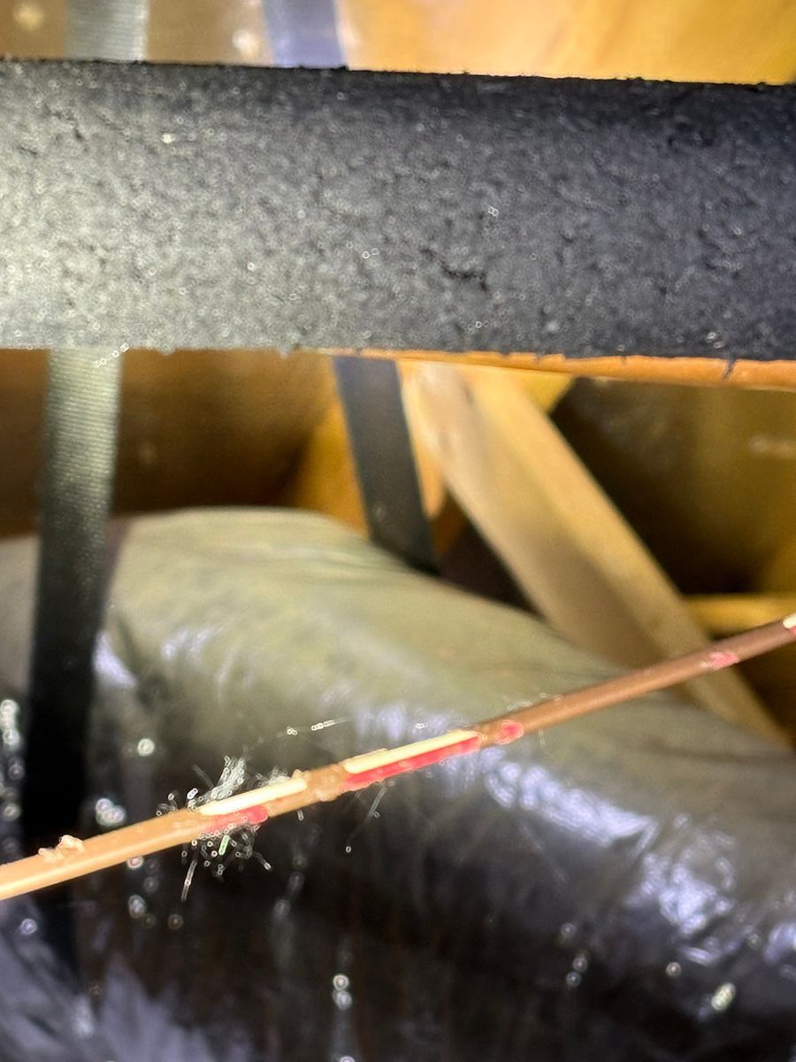 Insulation and wooden beams in an attic with a dangling cable in the foreground