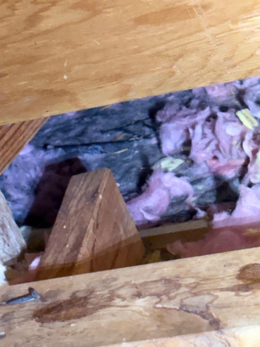 Open attic floor with exposed pink insulation and wooden beams under a plank