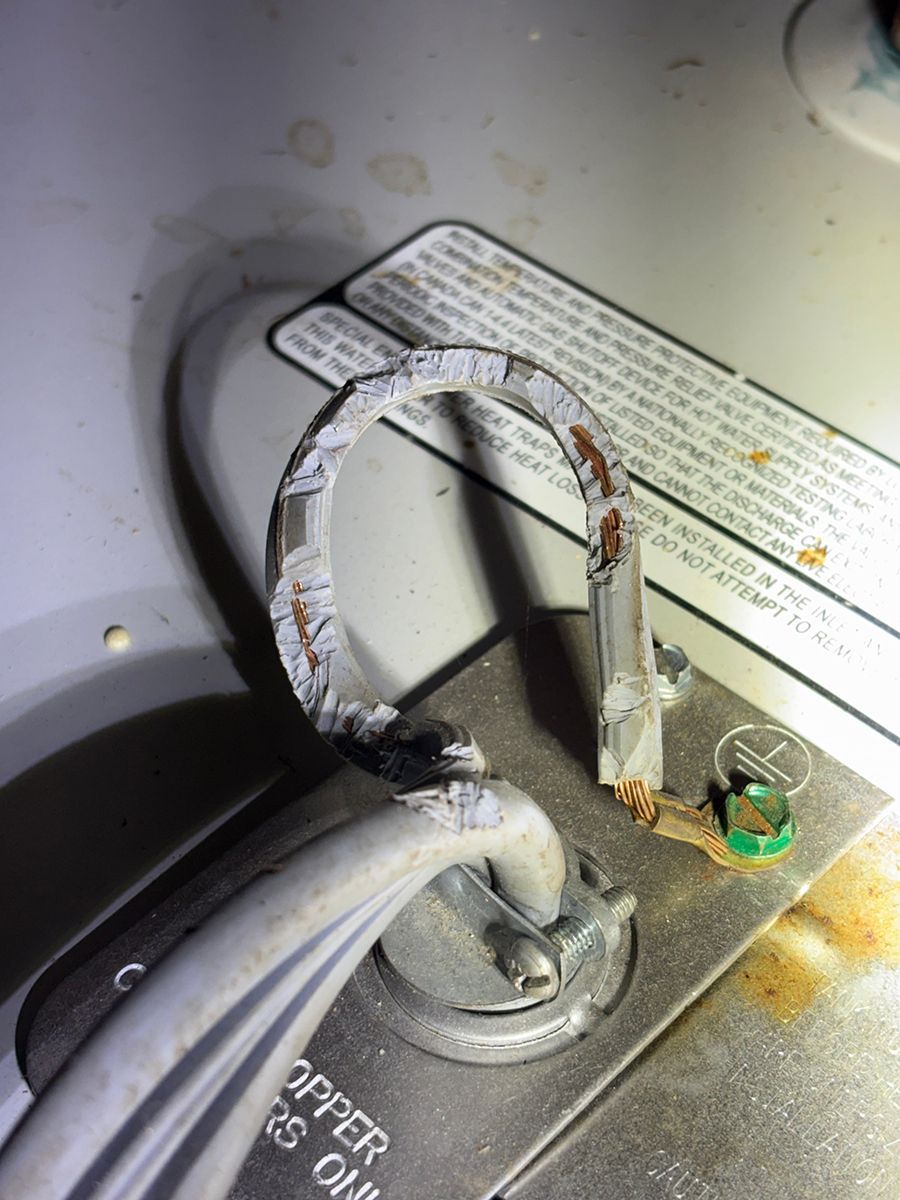 Corroded electrical wiring loop inside a metal appliance compartment, with a green ground screw visible