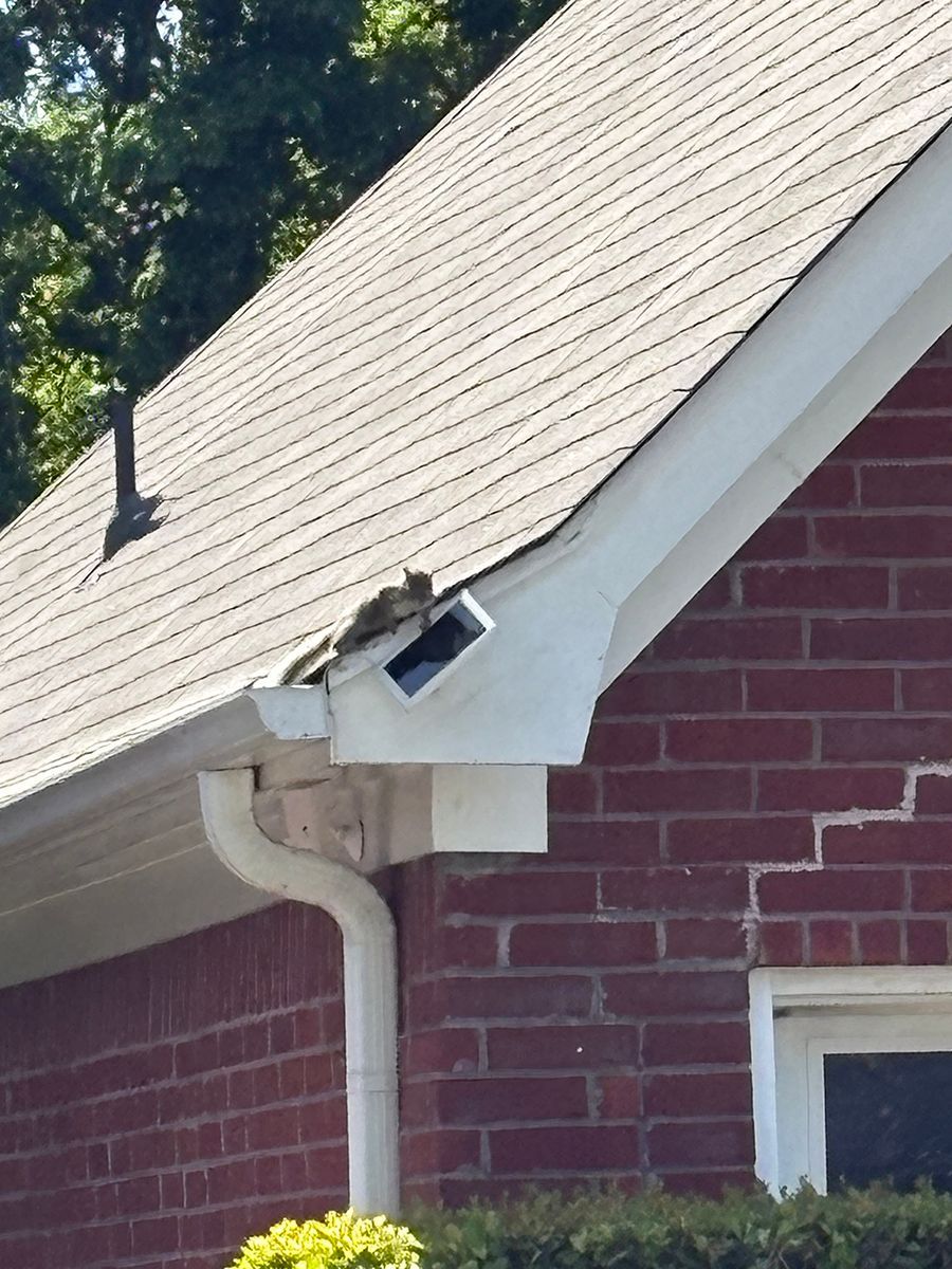 Damaged roof vent and gutter on a brick house under a sloped shingle roof