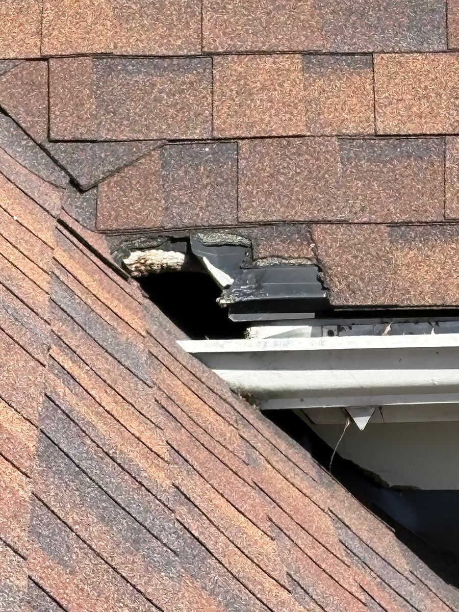 Damaged shingle roof with a large hole and exposed underlayment near a skylight