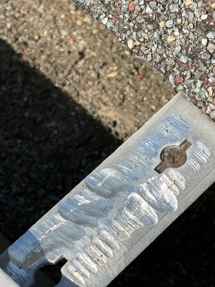 Close-up of a silver metal key with a worn, striped handle on pavement.
