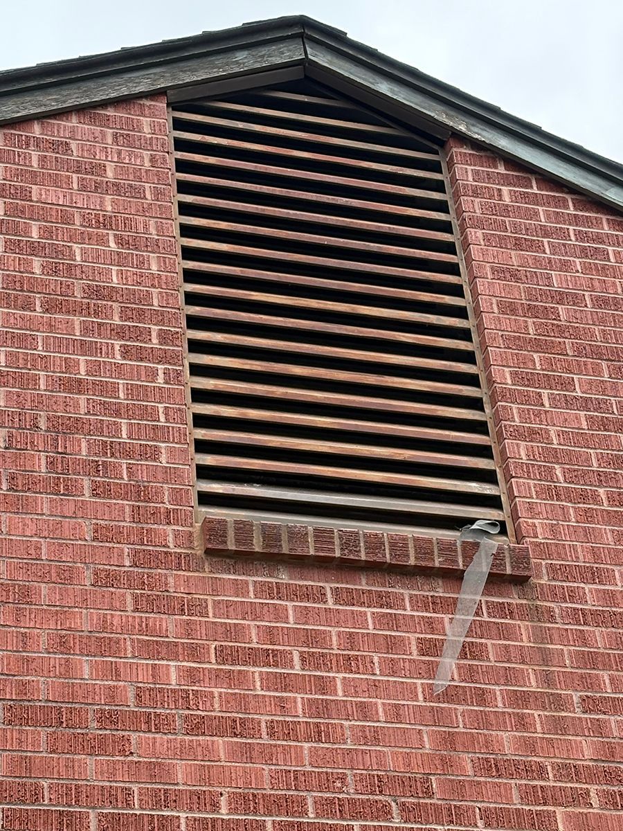 Brick building gable with black louvered vent and white downspout on the right side
