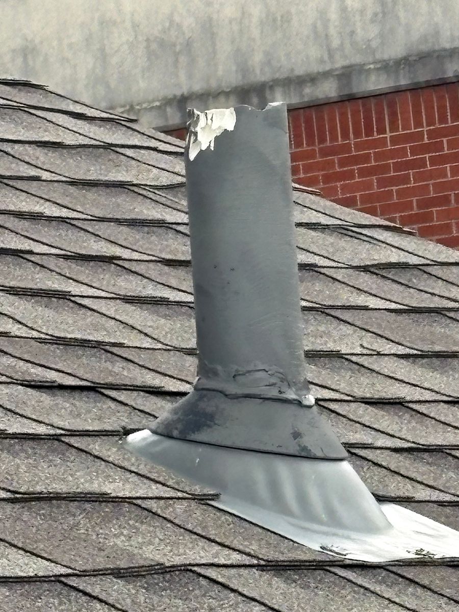 Damaged metal roof vent pipe on a shingled rooftop with peeling white paint.