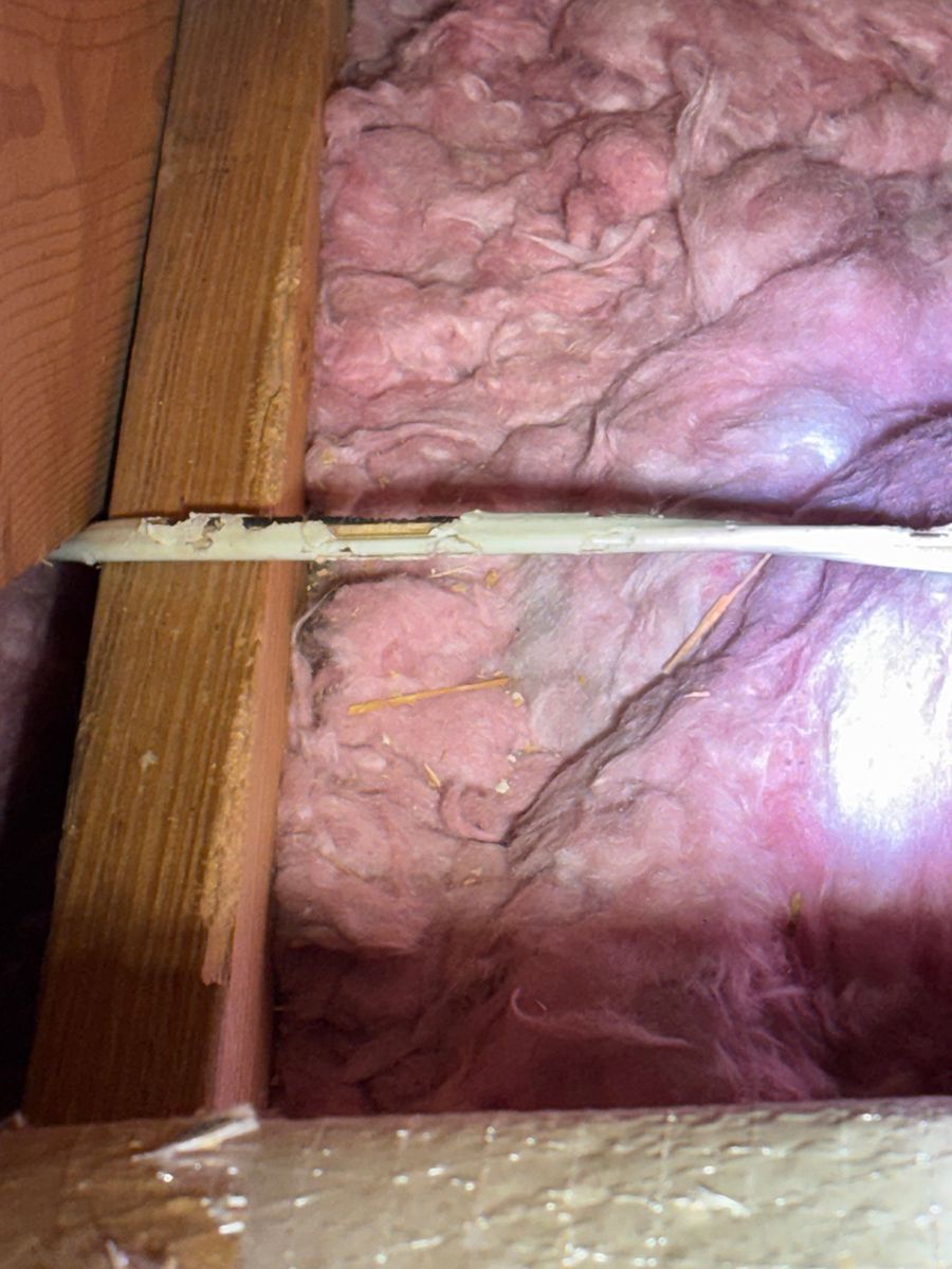 Insulation-filled wall cavity with a cable running between wooden studs and a bright light glare