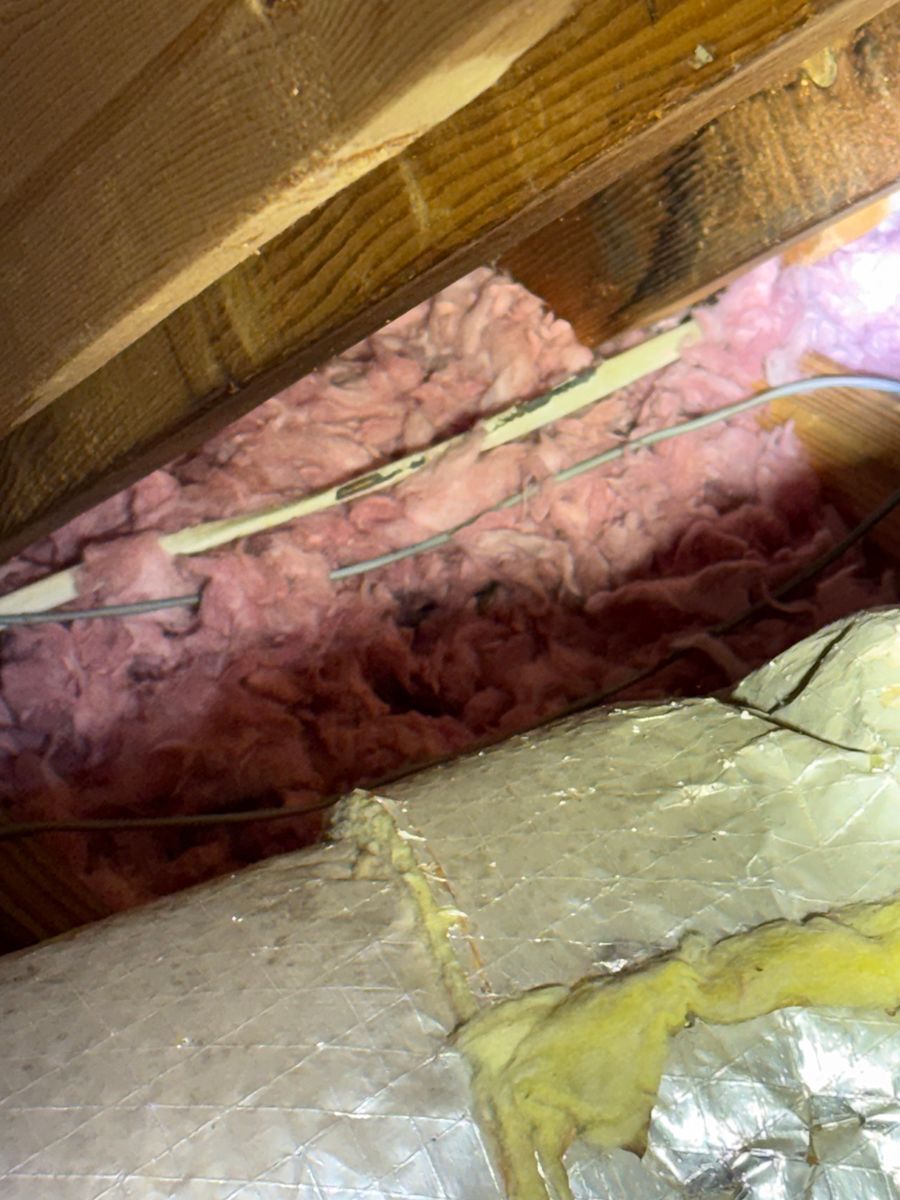 Insulation under wooden roof beams with pink and yellow fiberglass batts