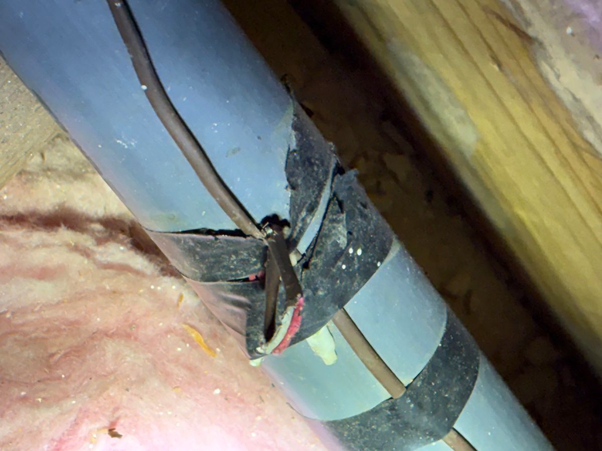 Damaged electrical cable with exposed wires between insulation and a wood beam