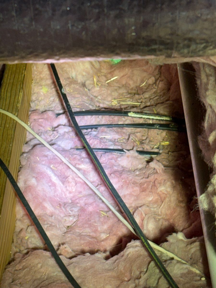 Exposed pink insulation and black cables in a narrow wall cavity beneath a wooden beam