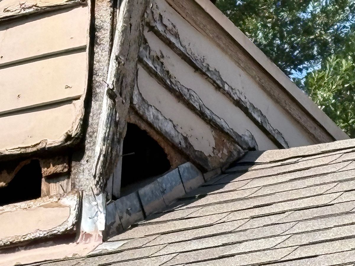 Damaged house roof with broken shingles and exposed opening near the peak
