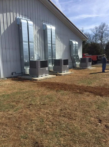 Three HVAC units sit against the side of a metal building with large external silver ductwork rising up the wall.