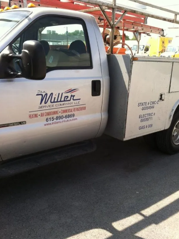 A silver Miller Service Company work truck with a utility body, ladders on the roof rack, and contact information.