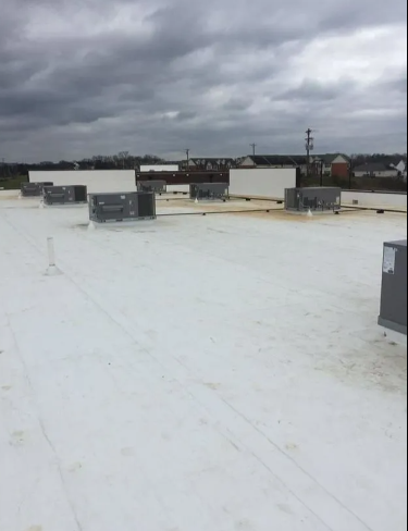 A wide-angle view of a flat, white roof featuring several grey HVAC units under a cloudy, overcast sky.