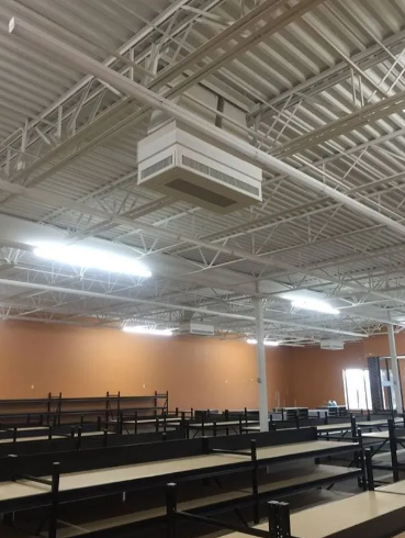 A wide shot of an empty retail space with tan walls, metal shelving, and industrial HVAC units suspended from the ceiling.