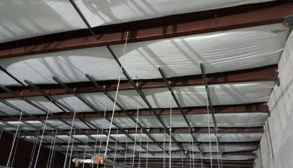 Industrial ceiling structure featuring dark metal beams, white insulation material, and vertical metal pipes.