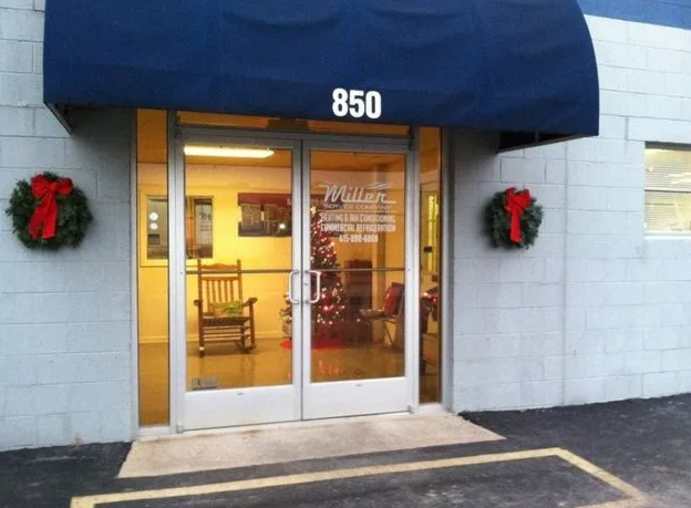 Building entrance 850 with a blue awning, glass double doors, two Christmas wreaths, and a rocking chair inside.