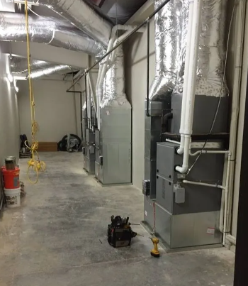 Three HVAC furnace units with silver insulated ductwork lined up against a wall in a utility room.