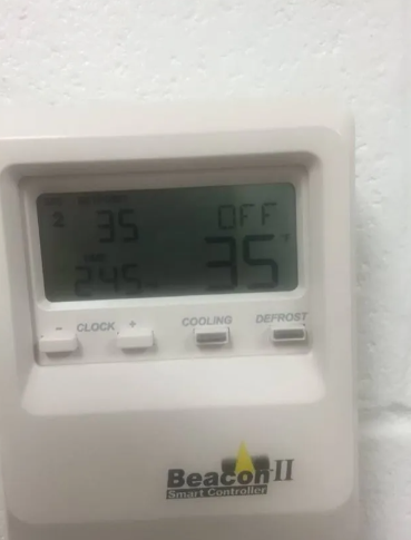 A white Beacon II smart controller on a white wall displays an 
