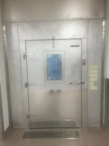 A metal, commercial-grade door with a central viewing window, diamond-plate kick plate, and a floor-level vent.