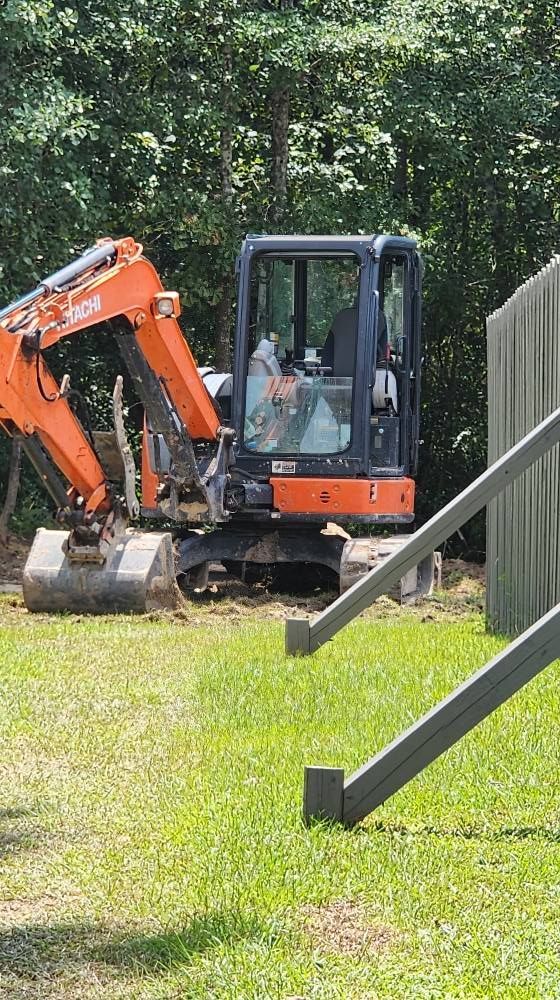 Orange excavator on a grassy area, near wooden stairs and trees.