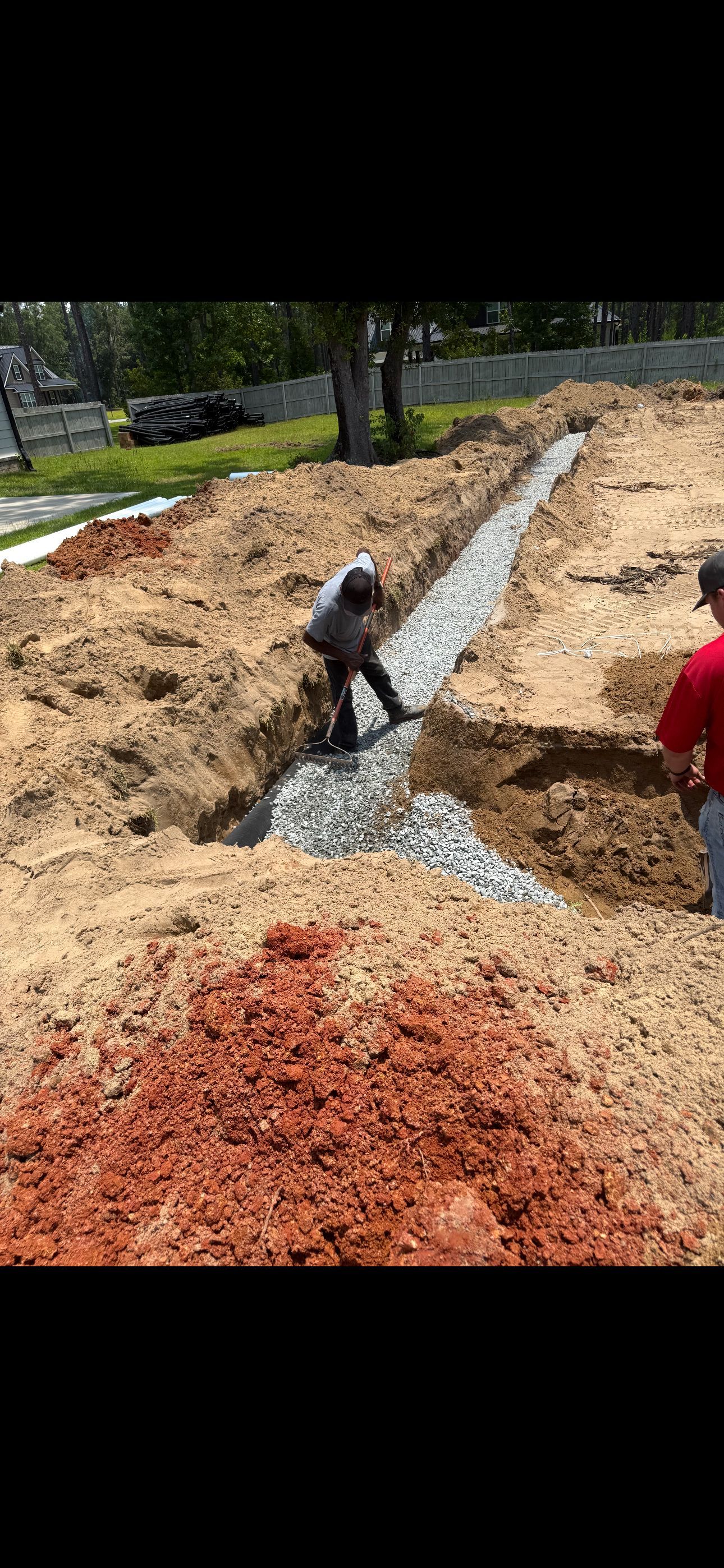 A person stands in a dirt trench filled with gravel during a construction project.