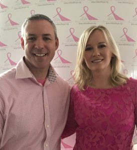 A man and a woman are posing for a picture in front of a wall with pink ribbons on it
