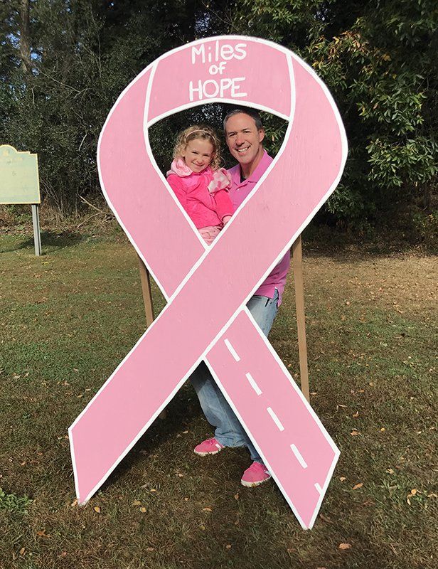 A man holding a little girl in front of a pink ribbon that says miles of hope
