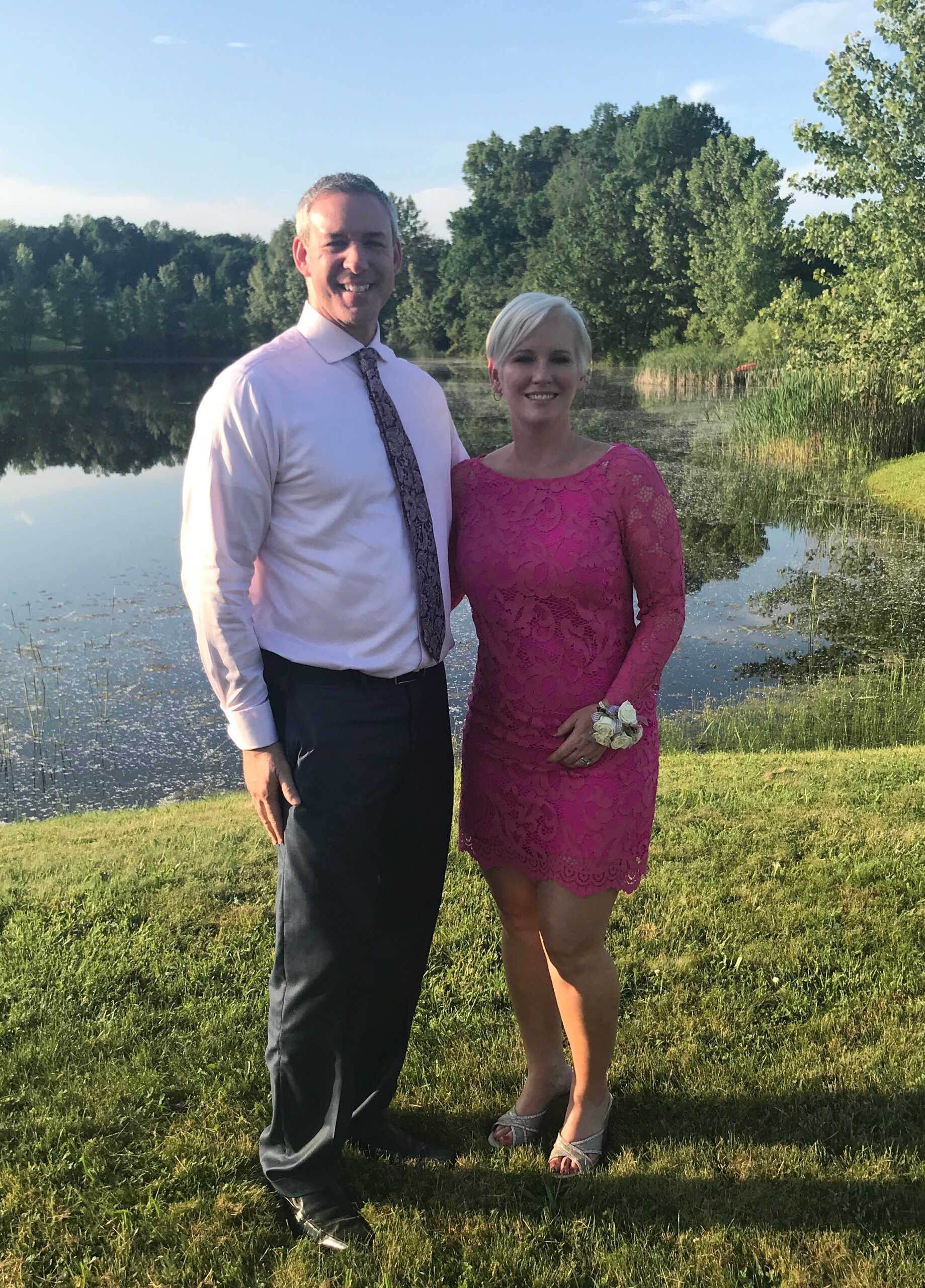A man and a woman are posing for a picture in front of a lake.