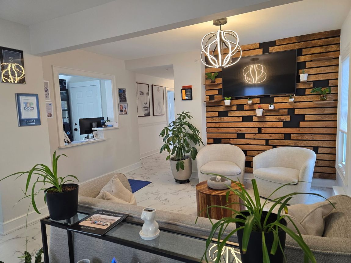 Waiting room with wooden accent wall, TV, white chairs, and potted plants.