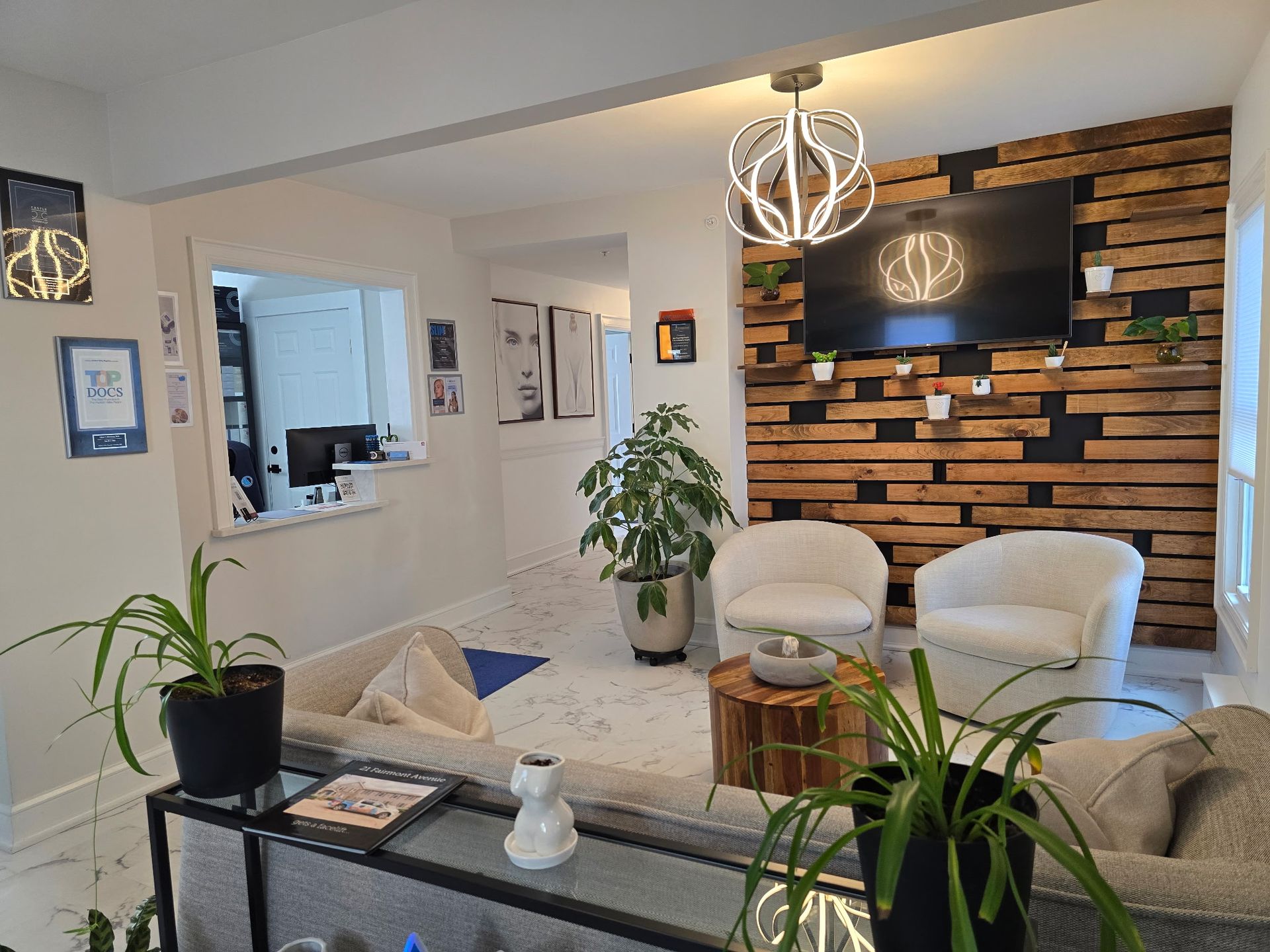 Waiting room with wooden accent wall, TV, white chairs, and potted plants.