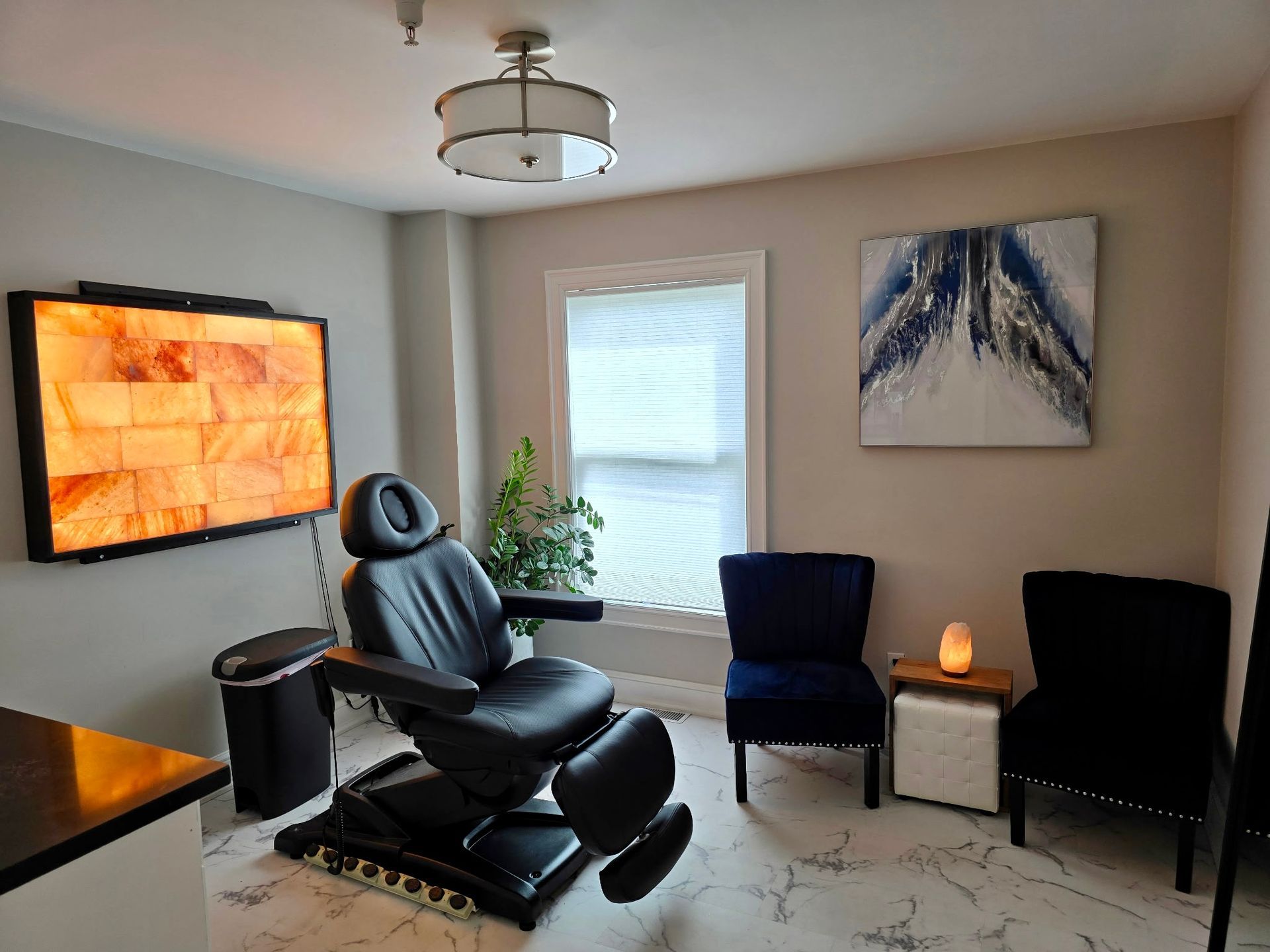 Relaxation room with treatment chair, salt lamp, blue velvet chairs, and art.