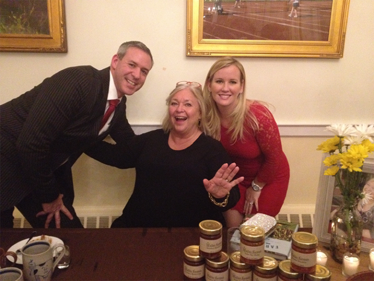 A man and two women are posing for a picture in front of jars of jam