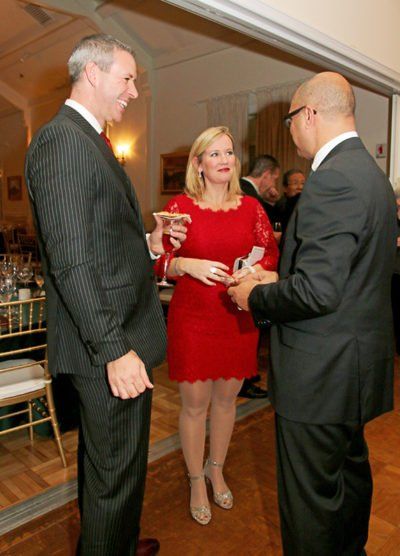A woman in a red dress is talking to two men in suits