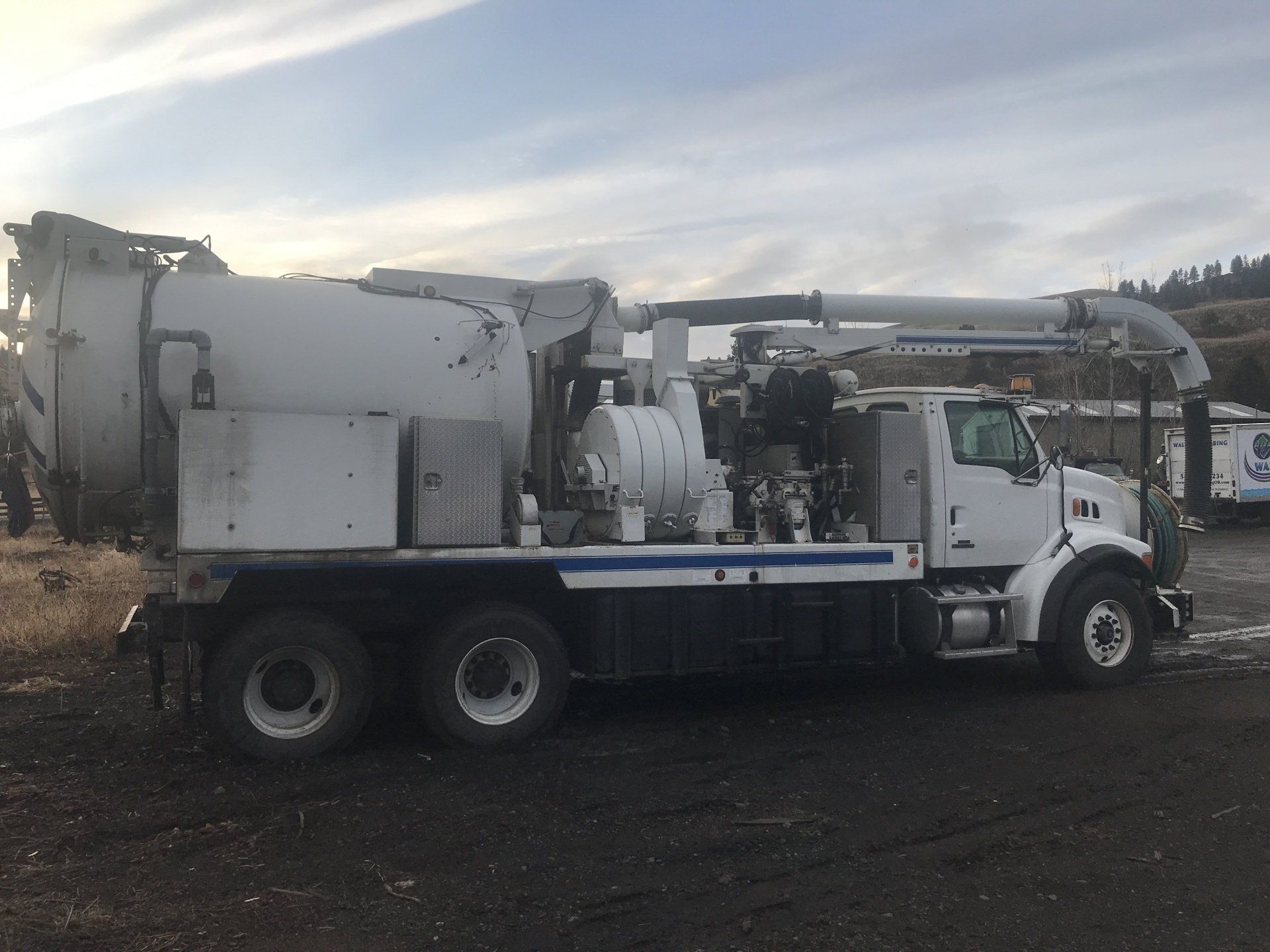 A white and blue vacuum truck is parked in a parking lot.