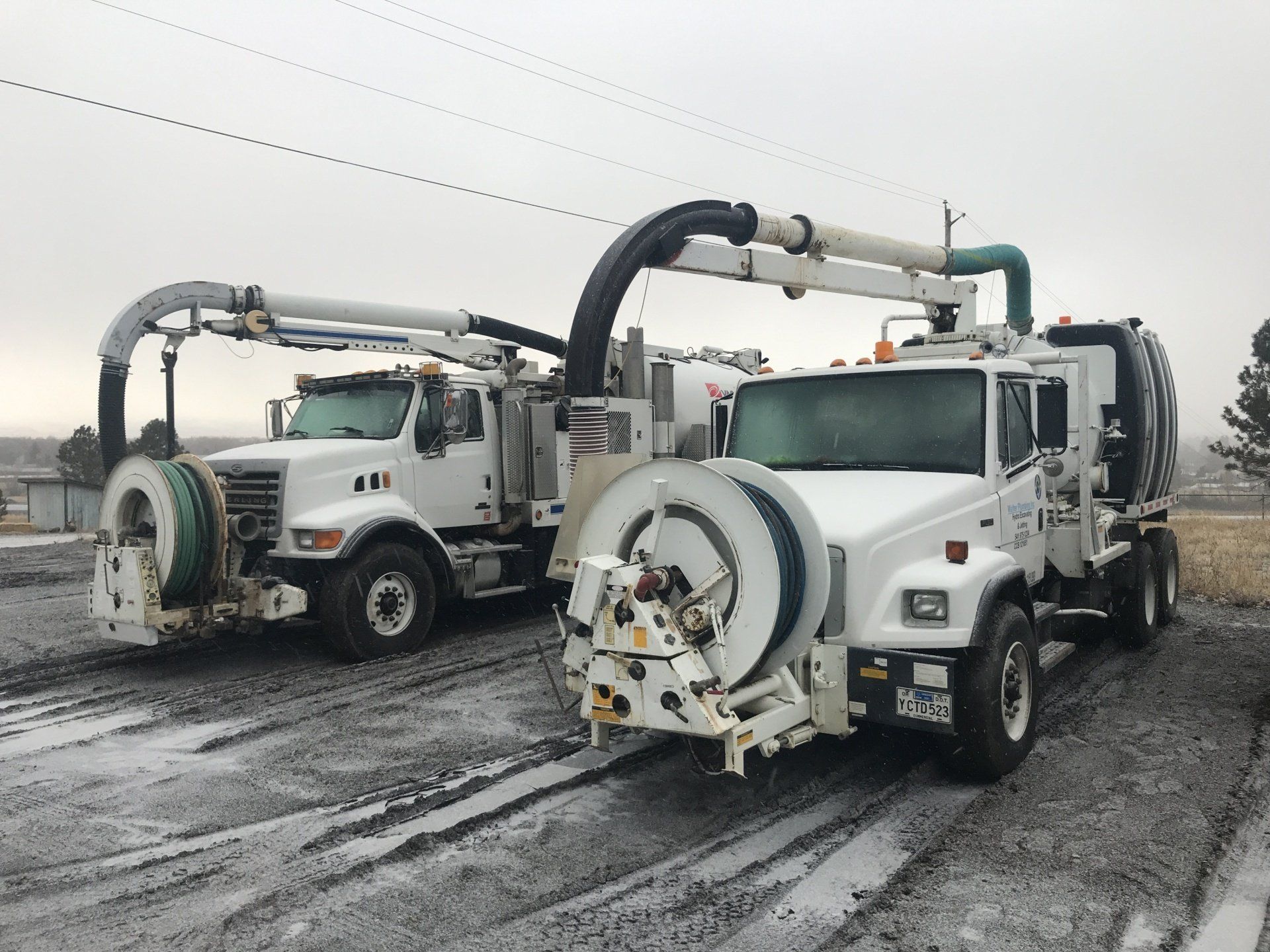 Two vacuum trucks are parked next to each other on a snowy road.