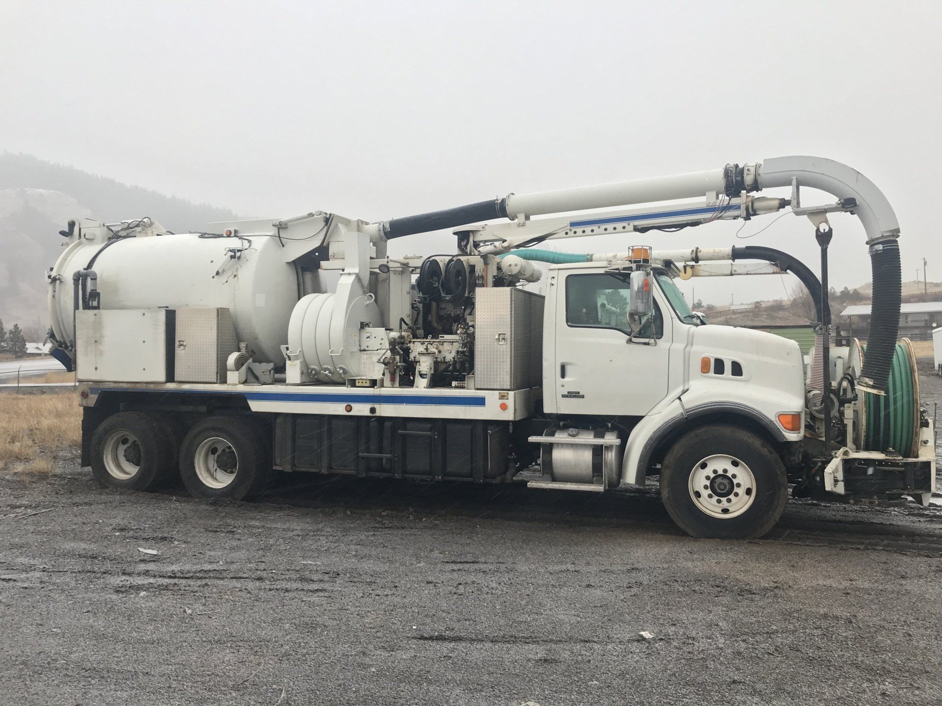 A white vacuum truck is parked in a gravel lot.